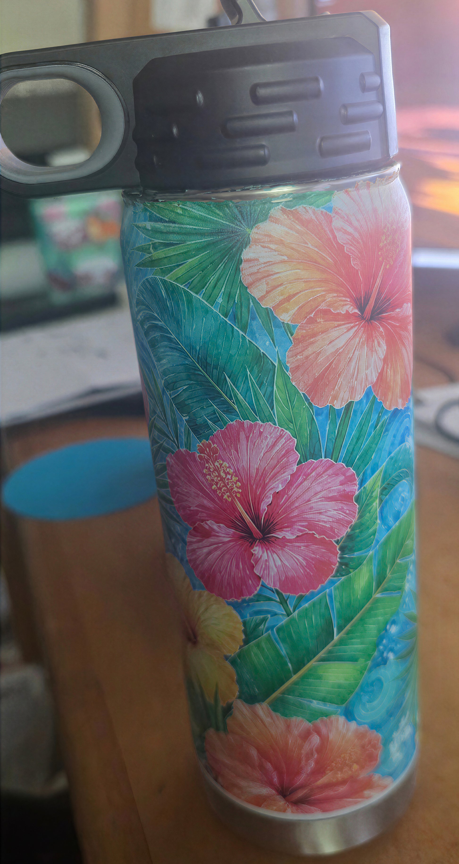 Front detail of the 20 oz bottle showing pink and coral hibiscus flowers, green leaves, turquoise background, and black lid.