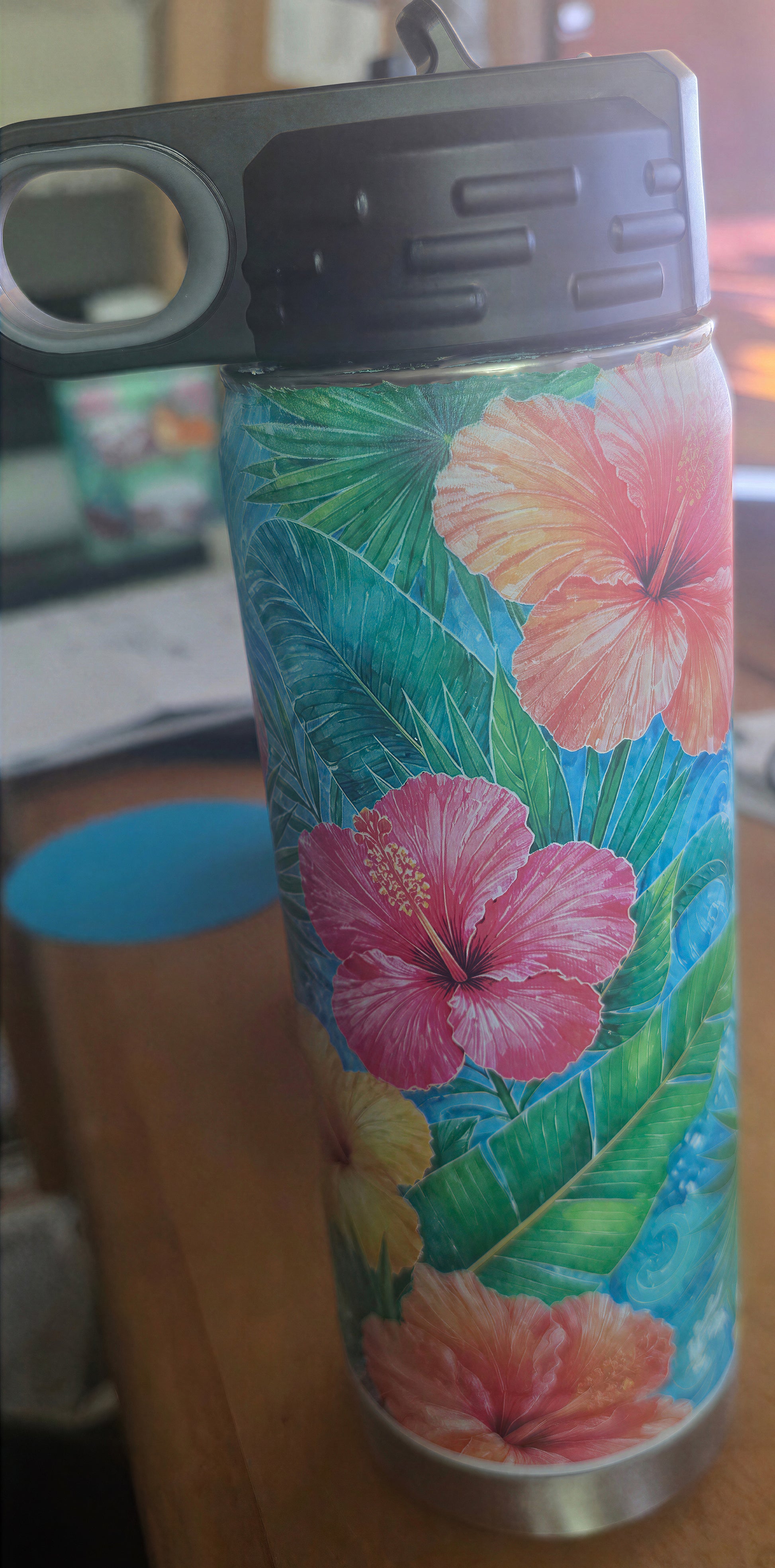 Close view of the hibiscus bottle artwork and black screw-on flip-top lid with finger opening.