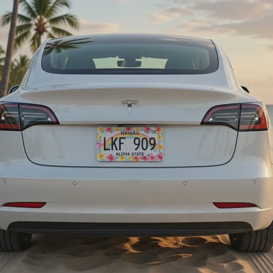 Watercolor plumeria license plate frame shown installed on a white car by a tropical beach