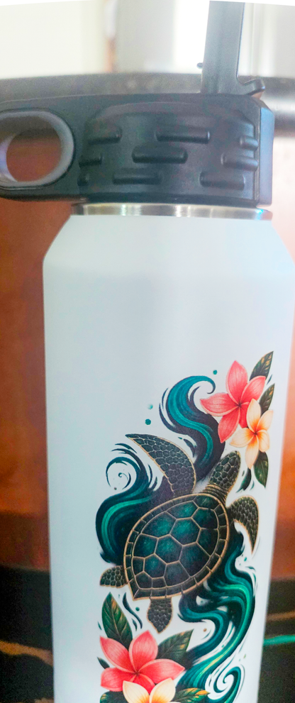 Close-up of the sea turtle and plumeria artwork on the white insulated bottle, stainless steel rim and black lid above