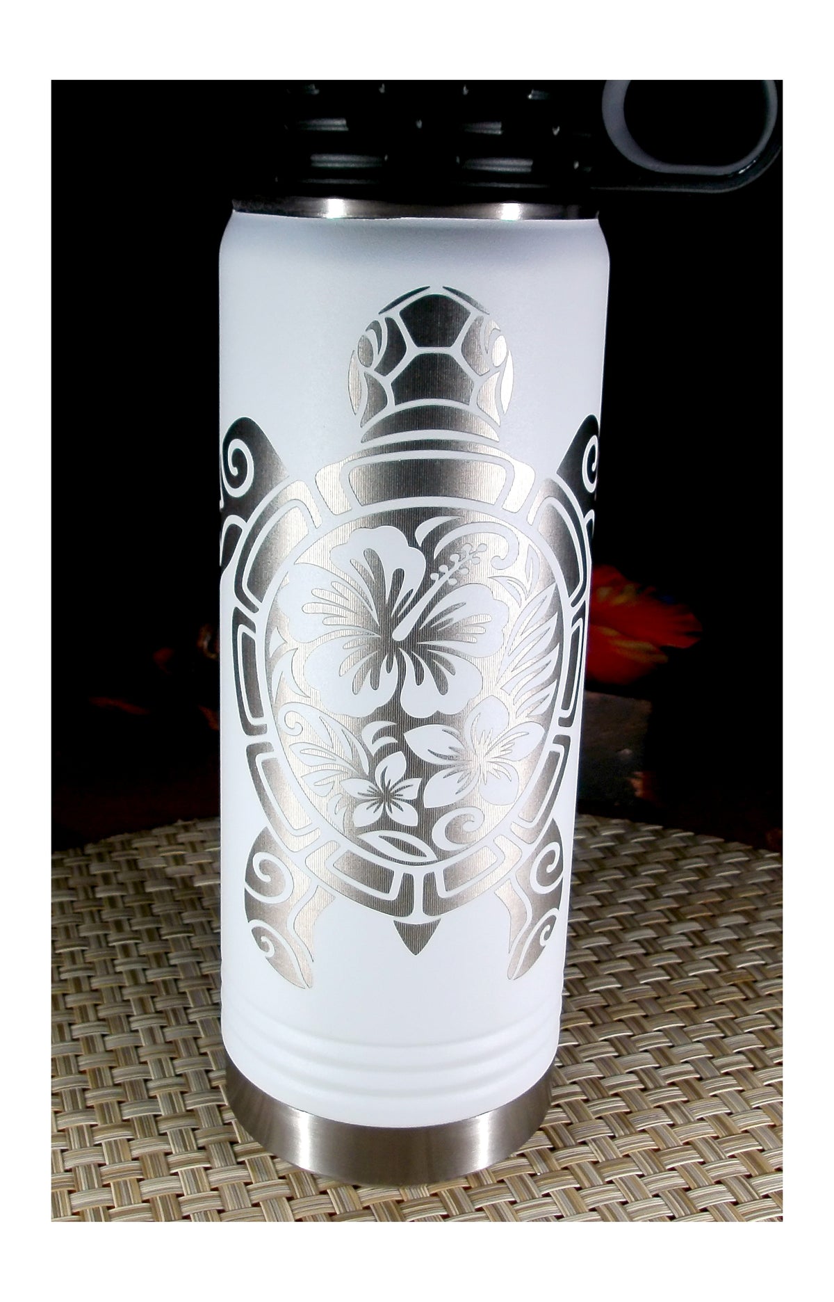 Front view of a white water bottle with silver engraved tribal sea turtle artwork filled with hibiscus and plumeria flowers.